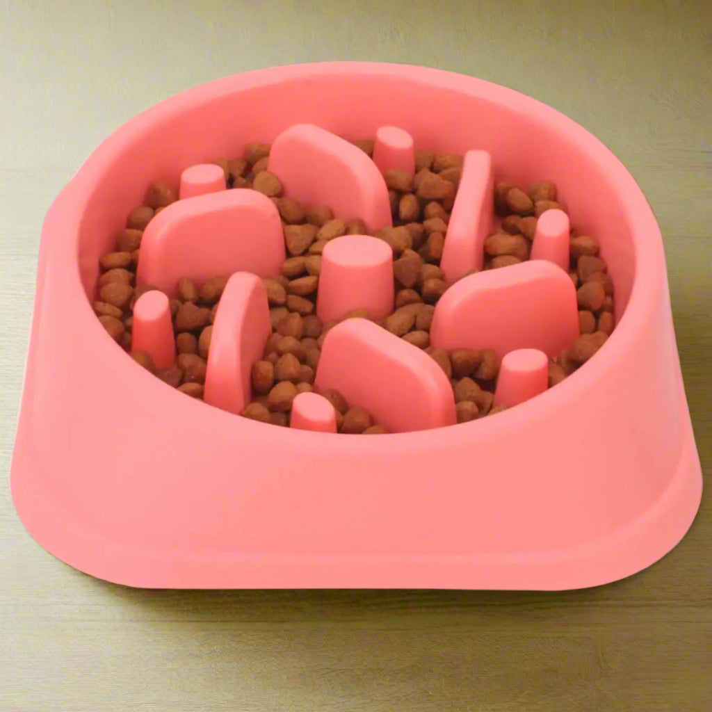 Pink pet feeding bowl with raised sections filled with kibble on a white background
